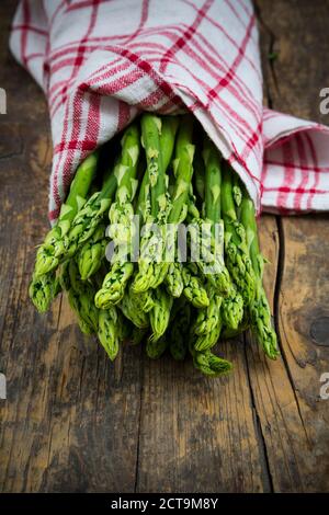 Bunch of green asparagus, Asparagus officinalis, wrapped in kitchen towel lying on dark wood Stock Photo