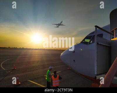 front of white commercial airplane standing on the airport runway at sunset.  Stock Photo