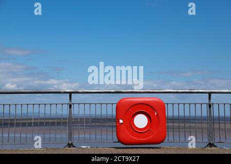 Life buoy in a red case hanging on railings at seashore. To save people in case of emergency. Stock Photo