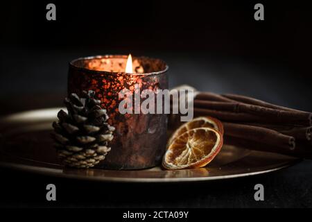 Christmas decoration with tea light candle, cinnamon sticks, slices of dried oranges and cone on plate, studio shot Stock Photo