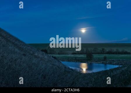 A full moon rises beside the huge Neolithic chalk mound of Silbury Hill, Avebury, Wiltshire, UK. It is 40m high and was built around 2300 BC Stock Photo