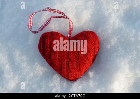 Red knitted heart lying on snow, close-up Stock Photo