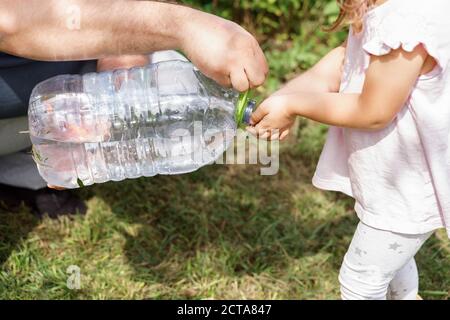 dad washes his child's hands from a bottle of water in the country Stock Photo