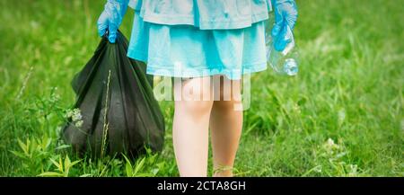 Little girl with crumpled plastic bottle and garbage bag in her hands while cleaning garbage in the park Stock Photo