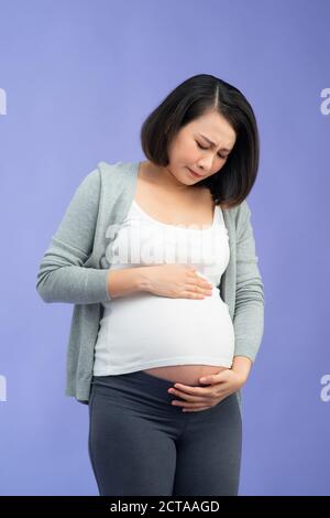 Pregnant lady suffering from abdomen pain touching belly standing on lilac background Stock Photo