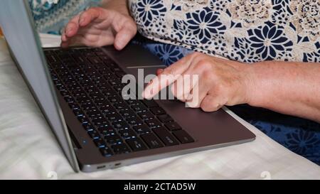 elderly woman is typing on a laptop. Close-up of hands and keyboard. Stock Photo