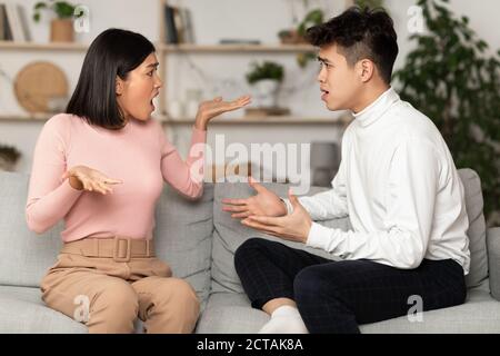 Chinese Couple Having Quarrel Arguing Sitting On Couch At Home Stock Photo