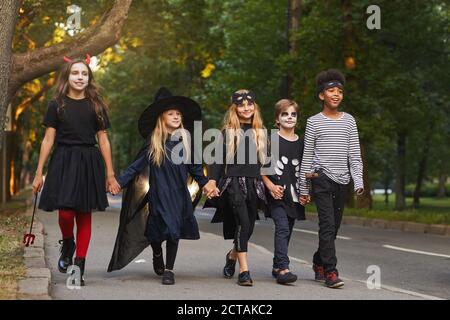 Full length portrait of multi-ethnic group of kids walking in street while trick or treating on Halloween Stock Photo