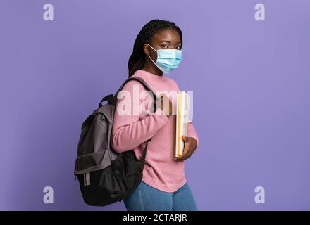 Education During Pandemic. Black Female Student In Protective Mask On Purple Background Stock Photo