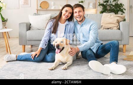 Young happy spouses with dog sitting in living room Stock Photo