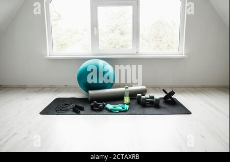 Empty modern white bright room with home workout accessories equipment. Yoga ball, resistance exercise latex band, foam roller, weights, jump rope, wa Stock Photo