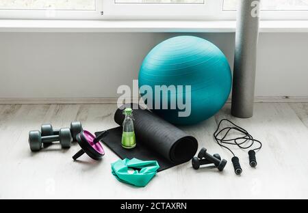 Empty modern white bright room with home workout accessories equipment. Yoga ball, resistance exercise latex band, foam roller, weights, jump rope, wa Stock Photo