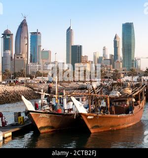 Arabic traditional wooden dhows in front of Kuwait skyscrapers in the beautiful evening light. Middle East, Kuwait City. Al Hamra Tower Stock Photo