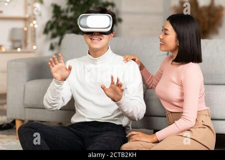 Asian Couple Using Virtual Reality Headset Having Fun At Home Stock Photo