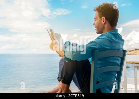 Relaxed man reading book at sea enjoying summer vacations on beautiful beach. Guy feeling free, relaxed and happy. Concept of vacations, freedom, happ Stock Photo