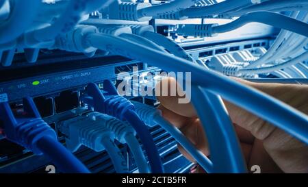 Macro Shot: IT Administrator Plugs in RJ45 Internet Connector into LAN Router Switch. Information Communication Network in Data Center with Cables Con Stock Photo