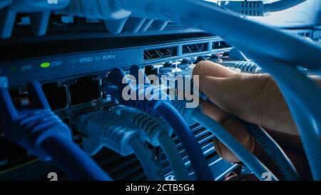 Macro Shot: IT Administrator Plugs in RJ45 Internet Connector into LAN Router Switch. Information Communication Network in Data Center with Cables Con Stock Photo