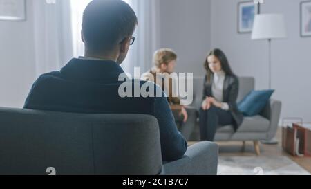 Unfocused Couple on Counseling Session with Psychotherapist. Focus on Back of Therapist Taking Notes and Talking: People Sitting on Analyst Couch Stock Photo