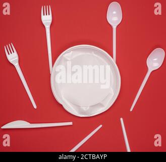round plate and stack of plastic forks and spoons on red background, top view Stock Photo