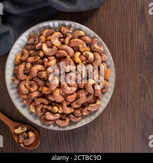 Cashew nuts with peel in a plate on wooden tray and table background, healthy raw food plate. Stock Photo