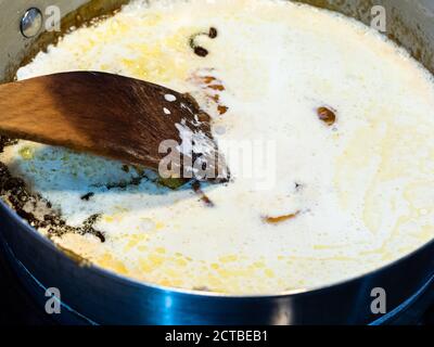 cooking salted butter caramel sauce at home kitchen - mixture of melted sugar and butter with added cream in steel pan close up Stock Photo