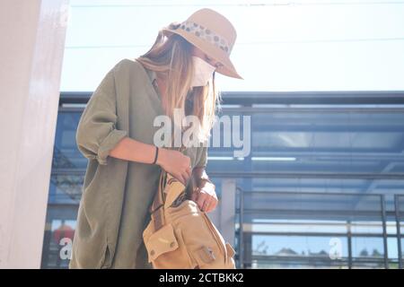 Young woman wearing face mask looking for something on her handbag. Coronavirus concept. Stock Photo