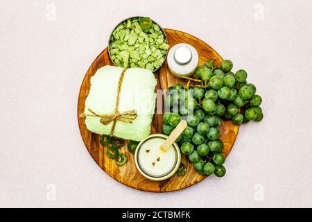 Natural spa accessories and green grapes placed on a wooden plate. Fresh ingredients for healthy and comfortable self care. Stone concrete background, Stock Photo