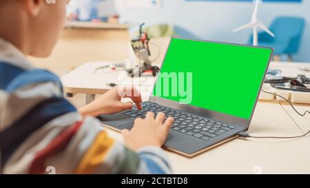 Elementary School Computer Science Classroom: Over the Shoulder View of a Kid Using Green Chroma Key Screen Laptop to Program Software for Robotics Stock Photo