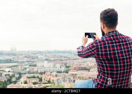 back view of a man taking a photo with his mobile phone of the city views from a rooftop, concept of freedom and technology, copy space for text Stock Photo