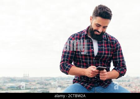 portrait of a handsome bearded man typing a text message on his mobile phone, concept of freedom and technology , copy space for text Stock Photo