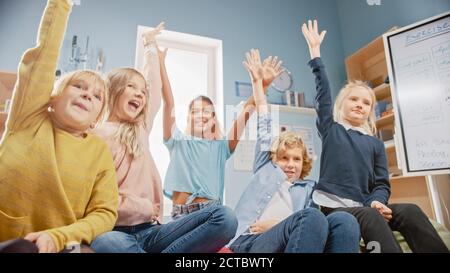 Elementary School Creativity Class: Diverse Children Sitting on the Carpet and Raising Hands with Ready Answer. Learning in Modern Environment. Low Stock Photo