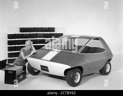 Publicity Photo for the Amitron, the American Motors Corporation and Gulton Industries electronic car powered by Gulton's long-life, light-weight lithium battery system. The AM prototype vehicle seen here is a  three-passenger car designed for short-haul transportation needs. The case in the foreground contains one-half of the lithium system, which is the equivalent in power to the 45 conventional automotive batteries, shown in the background, Detroit, MI, 1968. (Photo by RBM Vintage Images) Stock Photo