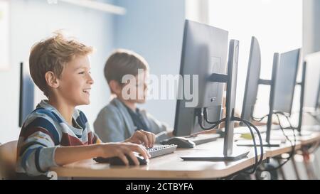 Elementary School Computer Science Classroom: Smart Little Schoolboy Works on Personal Computers, Learning Programming Language for Software Coding Stock Photo