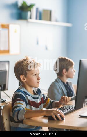 Elementary School Computer Science Classroom: Smart Little Schoolboy Works on Personal Computers, Learning Programming Language for Software Coding Stock Photo