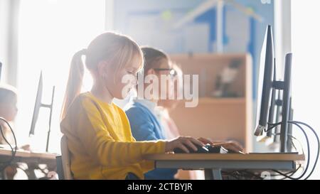 Elementary School Computer Science Classroom: Cute Little Girl Uses Personal Computer, Learning Programming Language for Software Coding Stock Photo