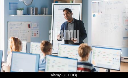 Elementary School Computer Science Class: Teacher Uses Digital Tablet, Explains Lesson to Diverse Group of Smart Children. Kids getting Modern Stock Photo