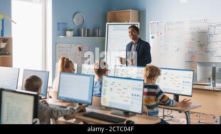 Elementary School Computer Science Class: Teacher Uses Digital Tablet, Explains Lesson to Diverse Group of Smart Children. Kids getting Modern Stock Photo