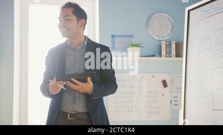 School Class: Portrait of the Enthusiastic and Motivated Teacher Using Digital Whiteboard and Tablet, Explains Lesson to Smart Children. Students Stock Photo