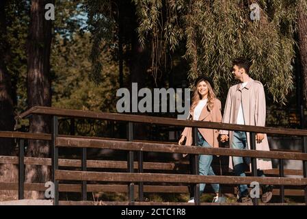 couple in trench coats holding hands and walking on wooden bridge Stock Photo