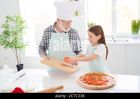 Photo of little girl granddaughter spend time aged granddad assistance put fresh cut ingredients on dough family pizza recipe cooking together friends Stock Photo