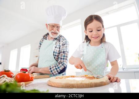 Portrait of his he her she nice cheerful focused grey-haired granddad grandchild cooking preparing flavoring fresh domestic delicious dish pizza Stock Photo