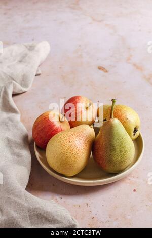 Seasonal apples and pears in a small plate on a pink marble backdrop with a beige linen napkin. Stock Photo