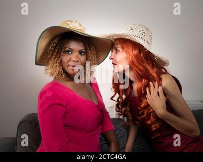 Horizontal portrait of two elegant and beautiful black and white women friends wearing summer hats Stock Photo