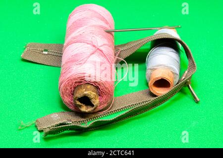 two spools of colored threads, a needle and a zipper on a green background Stock Photo
