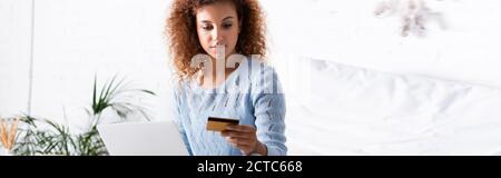 Panoramic crop of red haired woman holding credit card during online shopping at home Stock Photo