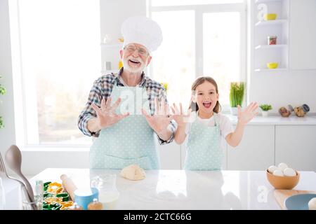 Portrait of nice cheerful cheery glad funny playful adorable grey-haired grandpa grandchild making domestic dough baking having fun showing palms Stock Photo