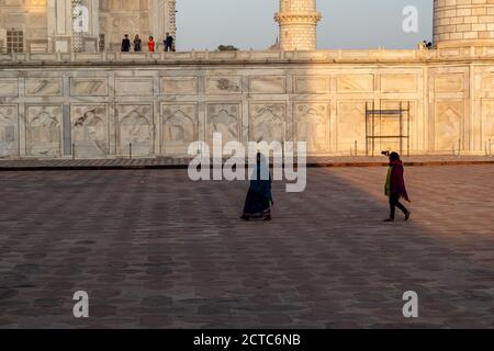 Agra, Uttar Pradesh, India - March 2019: Two Indian female tourists walk around the Taj Mahal taking pictures with their mobile phones. Stock Photo