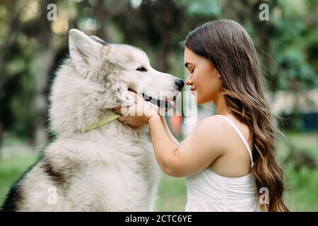 Young woman with innate disorder dwarfism embraces Malamute dog while walking in park. Portrait. Stock Photo