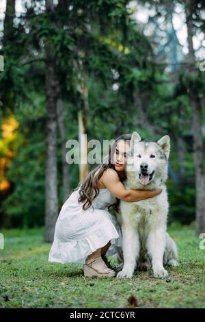 Young woman with innate disorder dwarfism embraces Malamute dog while walking in park. Stock Photo