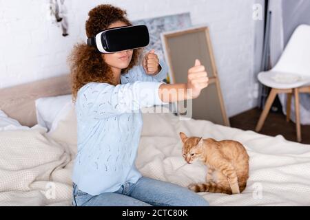Selective focus of woman playing video game in vr headset near cat in bedroom Stock Photo